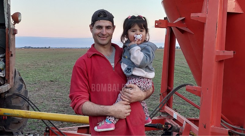 Matías con su pequeña hija, en el campo, detrás de un tractor.