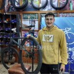 En el local donde atienden al público, Ramiro sostiene una rueda de bicicleta, sonriente.