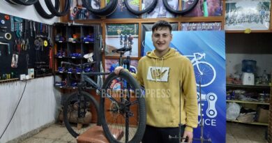 En el local donde atienden al público, Ramiro sostiene una rueda de bicicleta, sonriente.