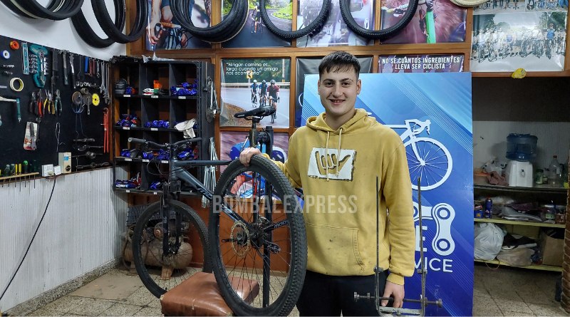 En el local donde atienden al público, Ramiro sostiene una rueda de bicicleta, sonriente.